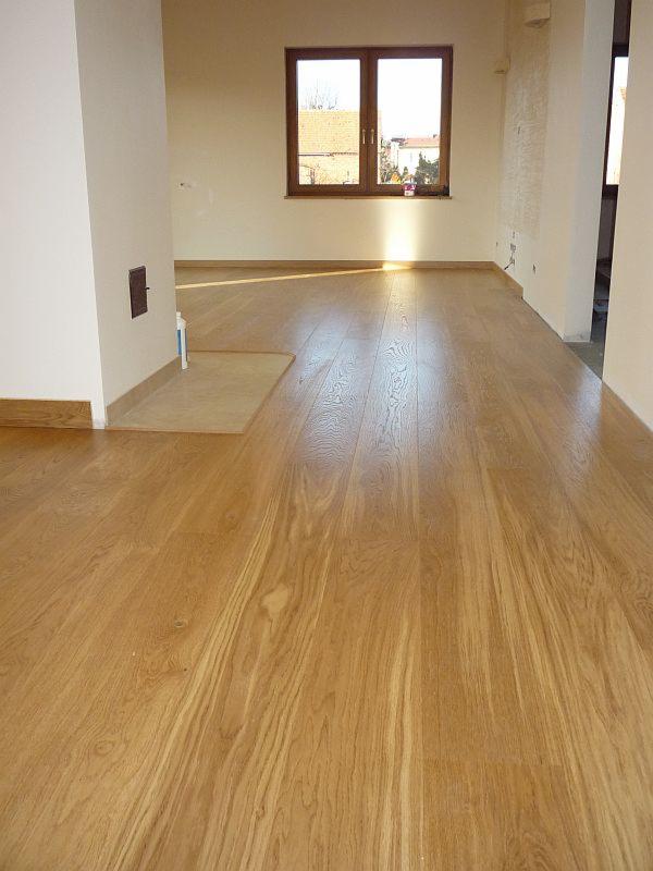 Jasny, drewniany parkiet ułożony w nowym, pustym pokoju z oknem; widoczny fragment podkładu pod parkiet w rogu pomieszczenia.