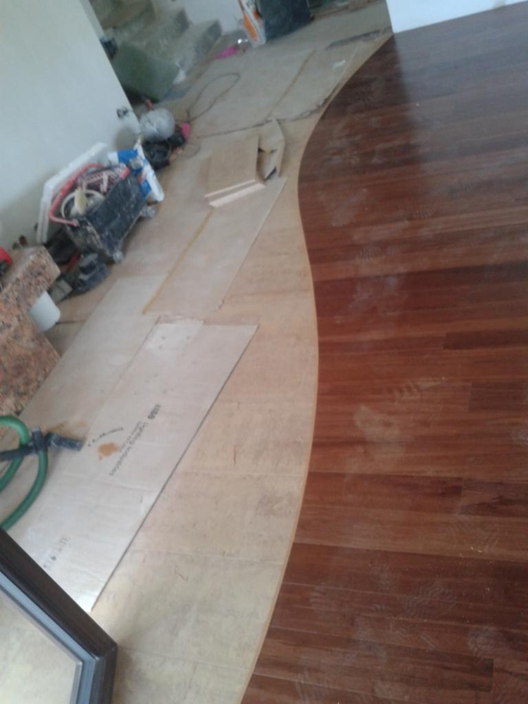 Połączenie parkietu z płytkami podłogowymi w łukowatym kształcie, widoczne narzędzia i materiały budowlane w tle, etap prac wykończeniowych.