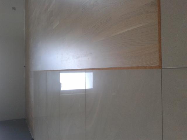 Połączenie parkietu z płytkami ceramicznymi na ścianie, widoczne przejście między materiałami, jasne kolory, minimalistyczny design.