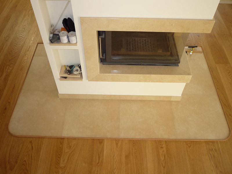 Wykończony fragment podłogi z płytek ceramicznych wokół kominka z drewnianą podłogą w tle, widoczne półki z akcesoriami obok kominka.