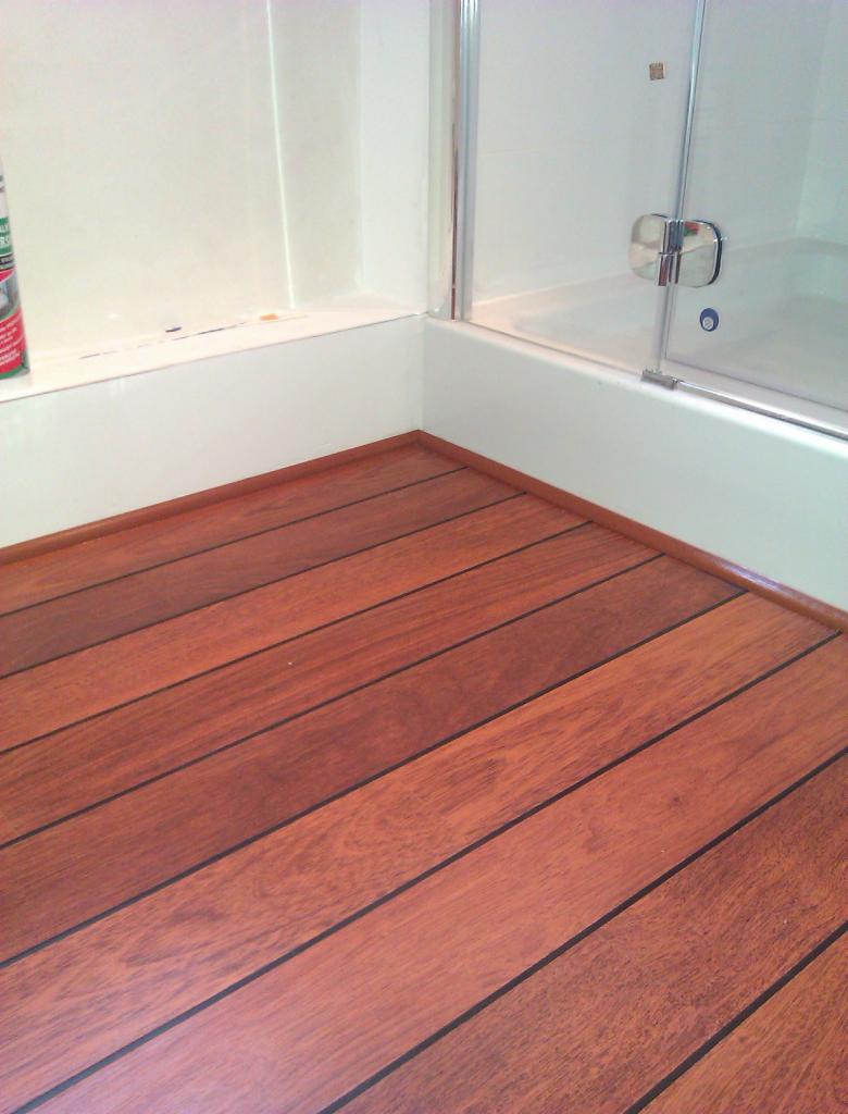 Nowa podłoga z paneli imitujących drewno w łazience, widok na kabinę prysznicową z chromowanymi elementami i białe ściany.