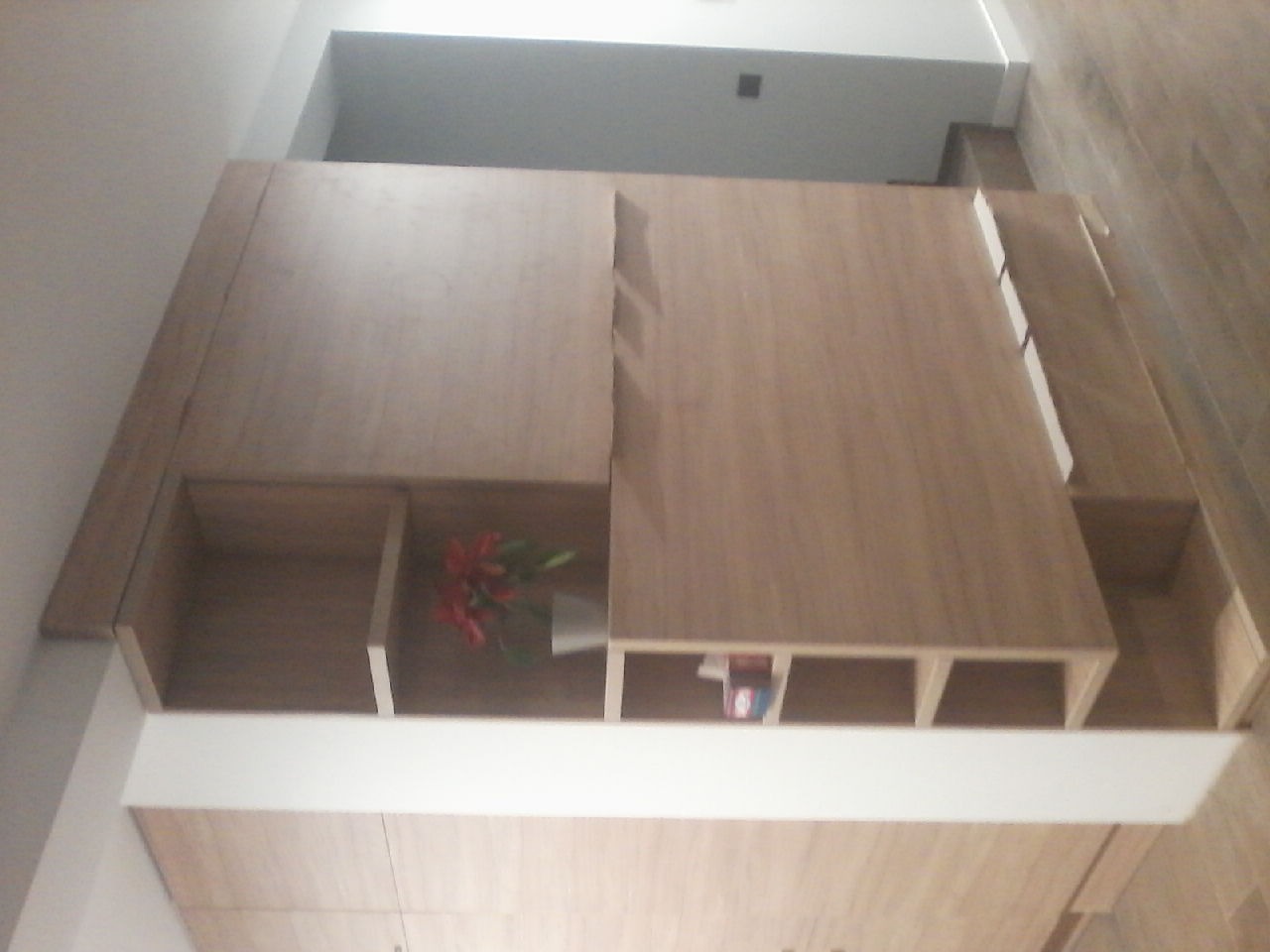 Wnętrze szafy z jasnego drewna z półkami, w jednej z nich wazon z czerwonymi kwiatami, widok z góry.