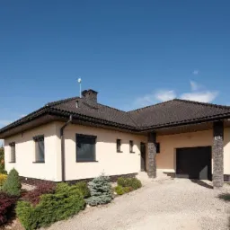 Parterowy dom jednorodzinny z ciemną dachówką i garażem, widoczny z przodu, z zadbanym ogrodem w tle, numer domu 62.