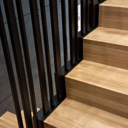 SŁAWKO-STAL - Nowoczesne schody z drewnianymi stopniami i czarną, metalową balustradą o minimalistycznym designie. Ujęcie z dołu, podkreślające geometrię i materiały.