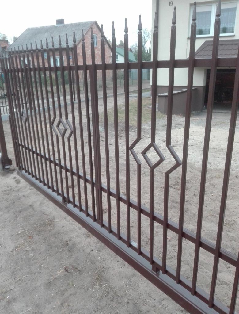Ciemnobrązowe, metalowe ogrodzenie panelowe z dekoracyjnymi rombami, widoczne na tle domu z numerem 19.