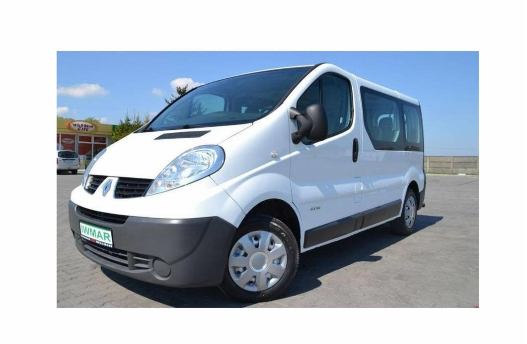 Biały Renault Trafic z ciemnymi szybami, zaparkowany na betonowym placu w słoneczny dzień, z widocznym szyldem 'Wild Bean Cafe' w tle.