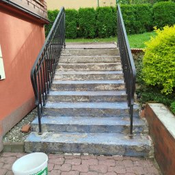 Damian Kanik Wykończenia wnętrz - Betonowe schody zewnętrzne z czarną metalową balustradą, widoczne ślady starej farby, obok wiadro i butelka z preparatem budowlanym.