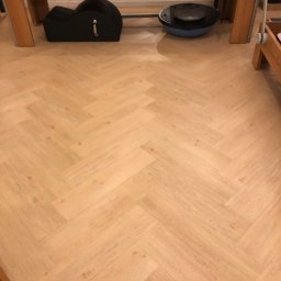 Damian Kanik Wykończenia wnętrz - Jasne panele ułożone we wzór jodełki francuskiej, widok z góry, na podłodze sprzęt do ćwiczeń pilates, oświetlenie ciepłe, bez widocznych listew przypodłogowych.