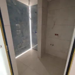 Wykończona łazienka z niebieskimi i szarymi płytkami. Widoczne instalacje wodne i elektryczne. Podświetlenie LED w strefie prysznica.