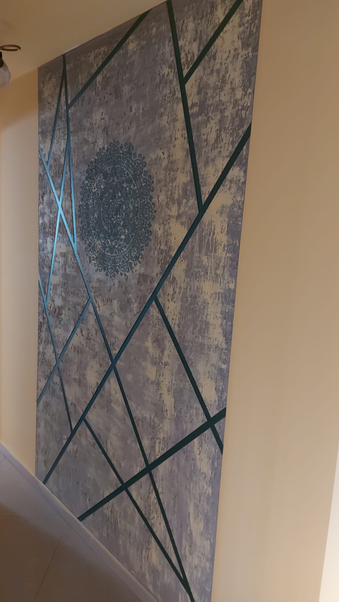 Dekoracyjna ściana z szarym tłem, geometrycznymi zielonymi liniami i okrągłym, ozdobnym motywem w centrum. Element wystroju wnętrza z bliska.