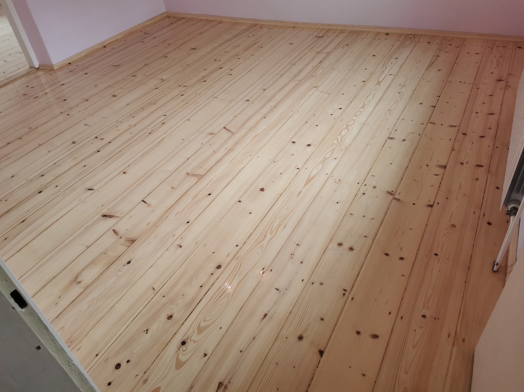 Jasna, odświeżona podłoga z desek po renowacji. Widoczne sęki i naturalny rysunek drewna. Świeżo położony lakier delikatnie odbija światło.