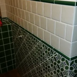 Wykończona łazienka z białymi i zielonymi płytkami o różnych wzorach, oddzielone ciemnozielonym pasem, widoczne detale fug i rolka papieru toaletowego.