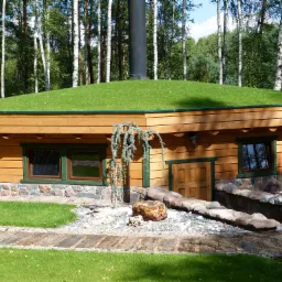 Drewniany budynek z zielonym dachem porośniętym trawą, z kominem, okna z zielonymi ramami, kamienna podmurówka i ścieżka z płyt.