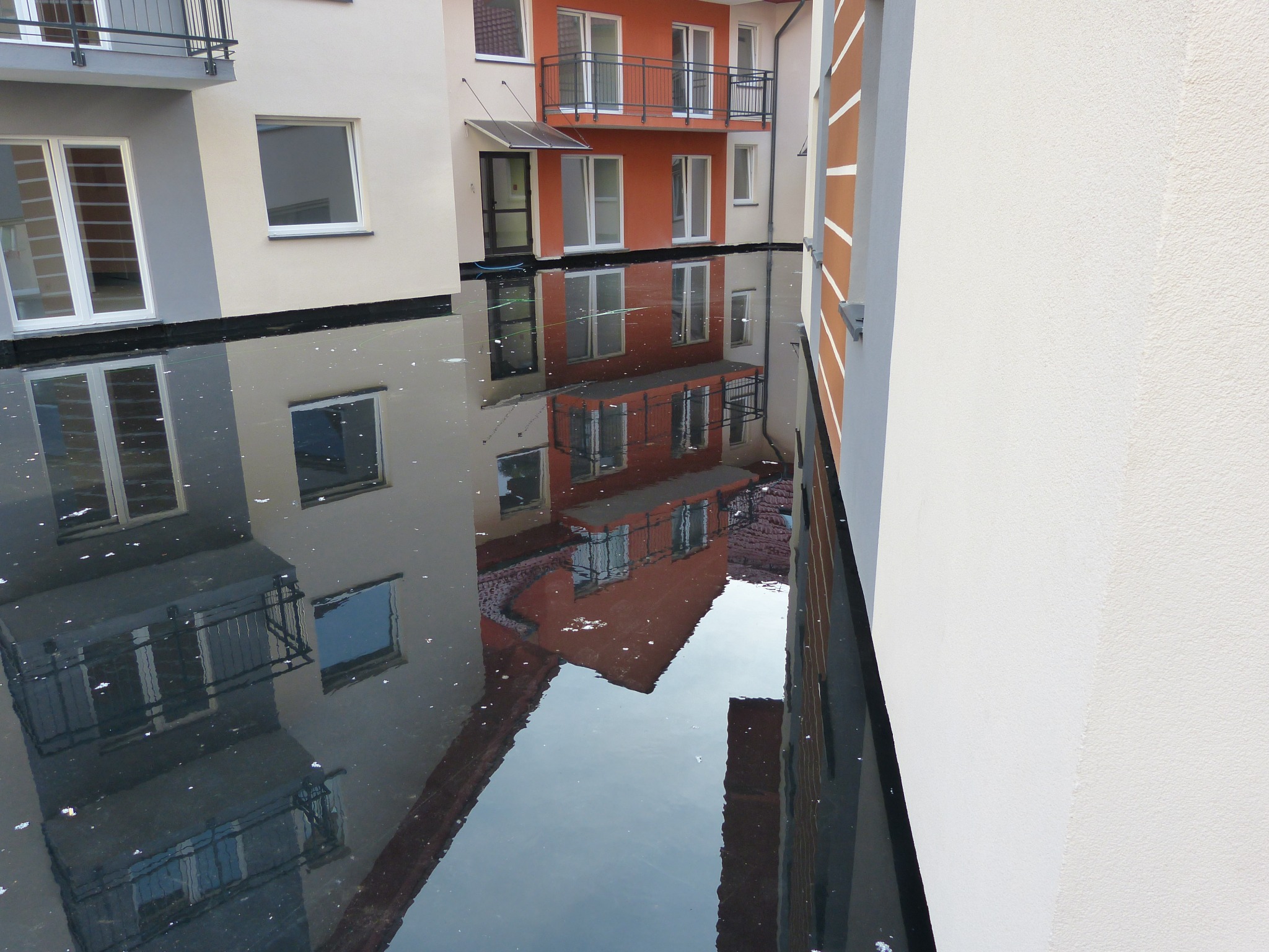 Budynki mieszkalne z balkonami odbijające się w kałuży na płaskim dachu, widok z góry.