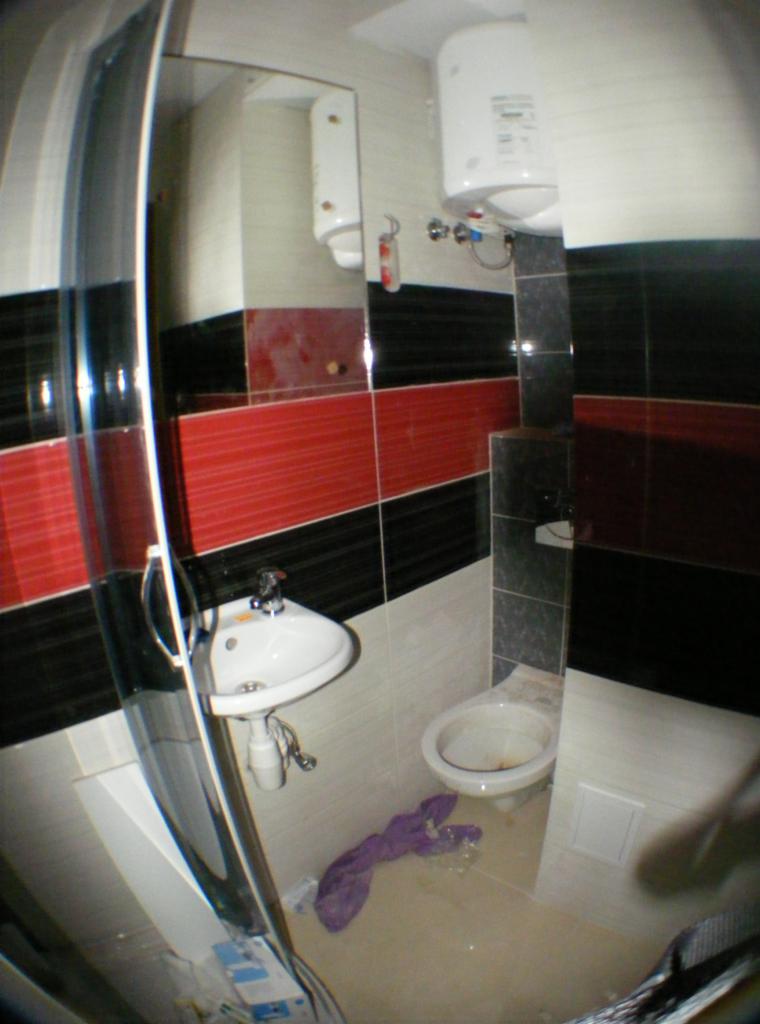 Niefortunne ujęcie łazienki po remoncie: widok na umywalkę, toaletę i bojler, z akcentami czerwono-czarnych płytek, ale z widocznymi niedociągnięciami i brakiem czystości.