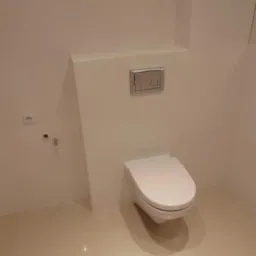 Nowoczesna toaleta podwieszana z białymi płytkami ceramicznymi na ścianach i podłodze, srebrny panel spłukujący, minimalistyczne gniazdko elektryczne i rurka doprowadzająca wodę.