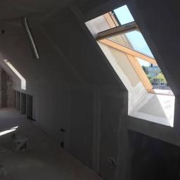 Pro-Bud system - Poddasze w trakcie prac wykończeniowych: widoczne okno dachowe z drewnianą ramą, ściany pokryte płytami gipsowo-kartonowymi przed szpachlowaniem, fragment instalacji wentylacyjnej pod sufitem...