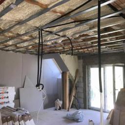 Pro-Bud system - Wnętrze w trakcie prac wykończeniowych: sufit z izolacją piankową, metalowa konstrukcja podwieszana, widoczne rury instalacyjne, ściany z płyt gipsowo-kartonowych, okno balkonowe i materiały...