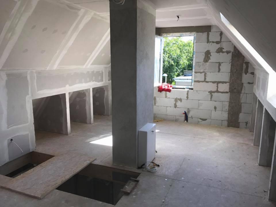 Surowe wnętrze poddasza w Brzegu w trakcie remontu, widoczne ściany z bloczków, płyty kartonowo-gipsowe, przygotowane otwory w podłodze i pion kanalizacyjny.
