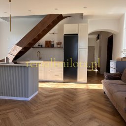 Remall Miłota Wykończenia - Jasne wnętrze po metamorfozie w Raciborzu: drewniana podłoga w jodełkę, schody z drewna, biała zabudowa kuchenna i wyspa. Nowoczesny design.