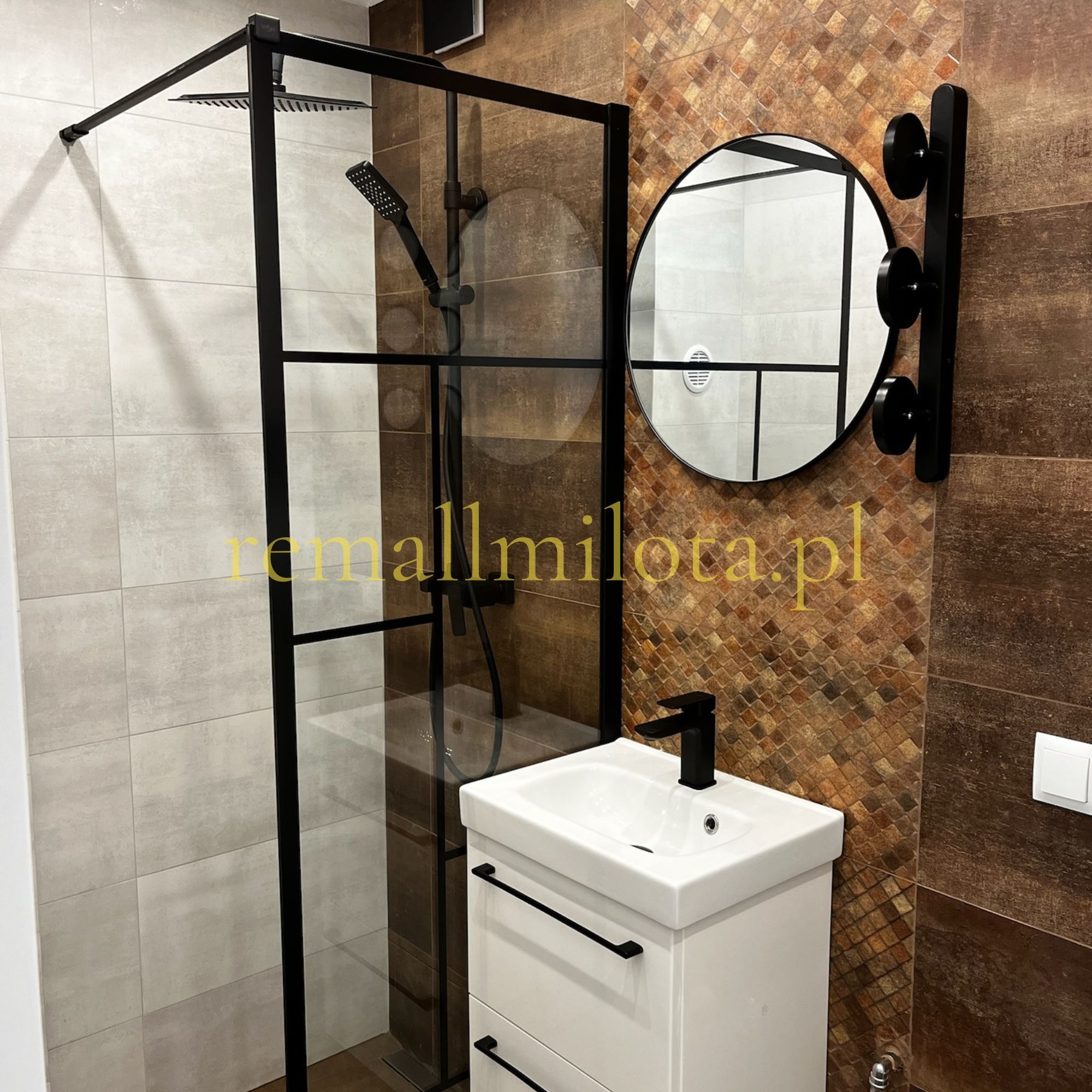 Nowoczesna łazienka po remoncie: kabina prysznicowa typu walk-in z czarnymi profilami, biała szafka z umywalką i okrągłe lustro z czarnym uchwytem na tle mozaiki.