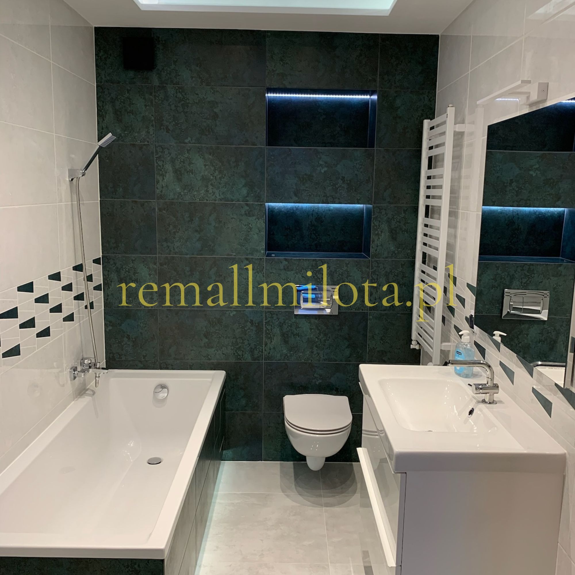 Nowoczesna łazienka z zielonymi płytkami, podświetlanymi niszami, białą armaturą i grzejnikiem drabinkowym. Minimalistyczny design z akcentami geometrycznymi.