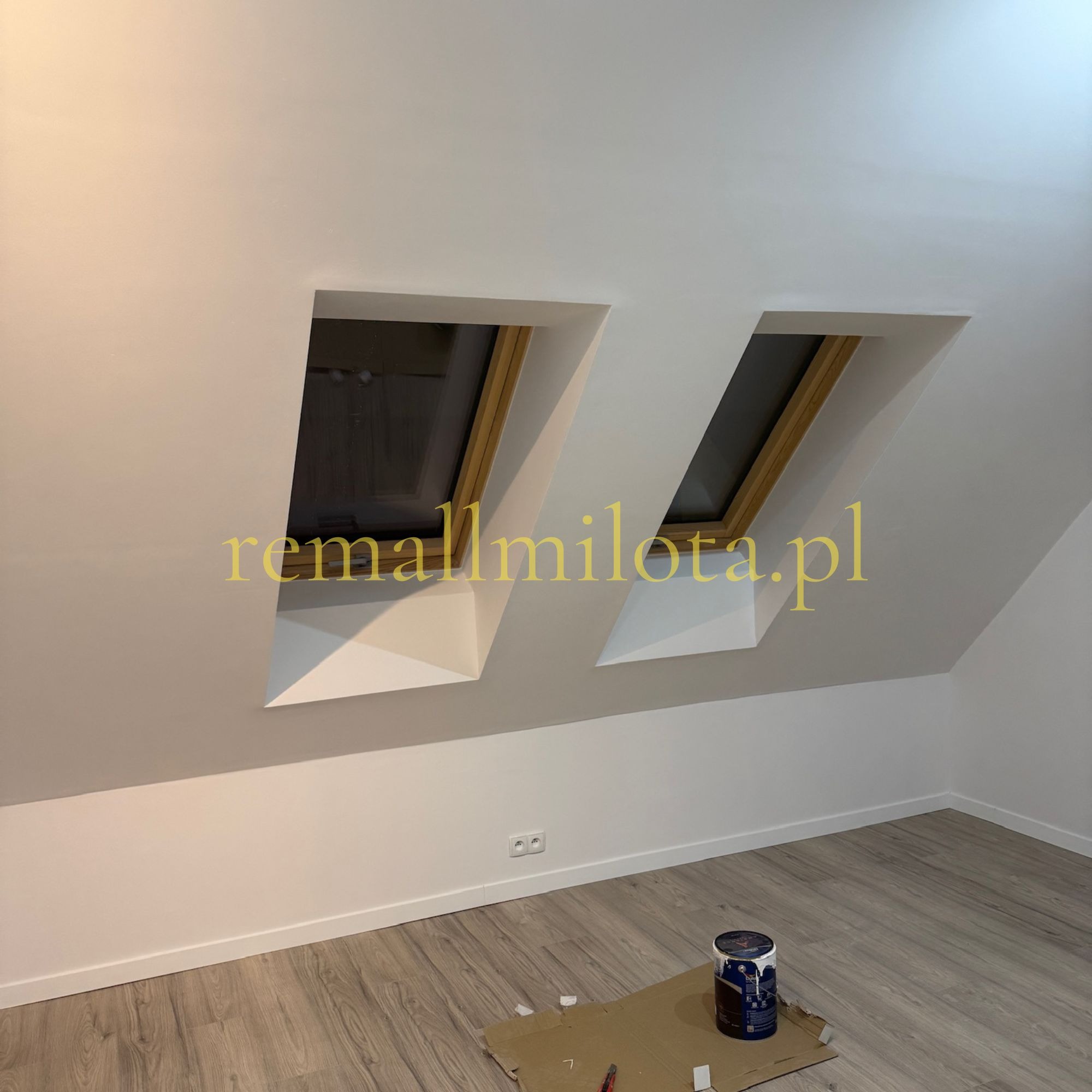 Poddasze po malowaniu na biało, dwa okna dachowe z drewnianą ramą, puszka farby na podłodze. Widok na świeżo odnowione wnętrze.