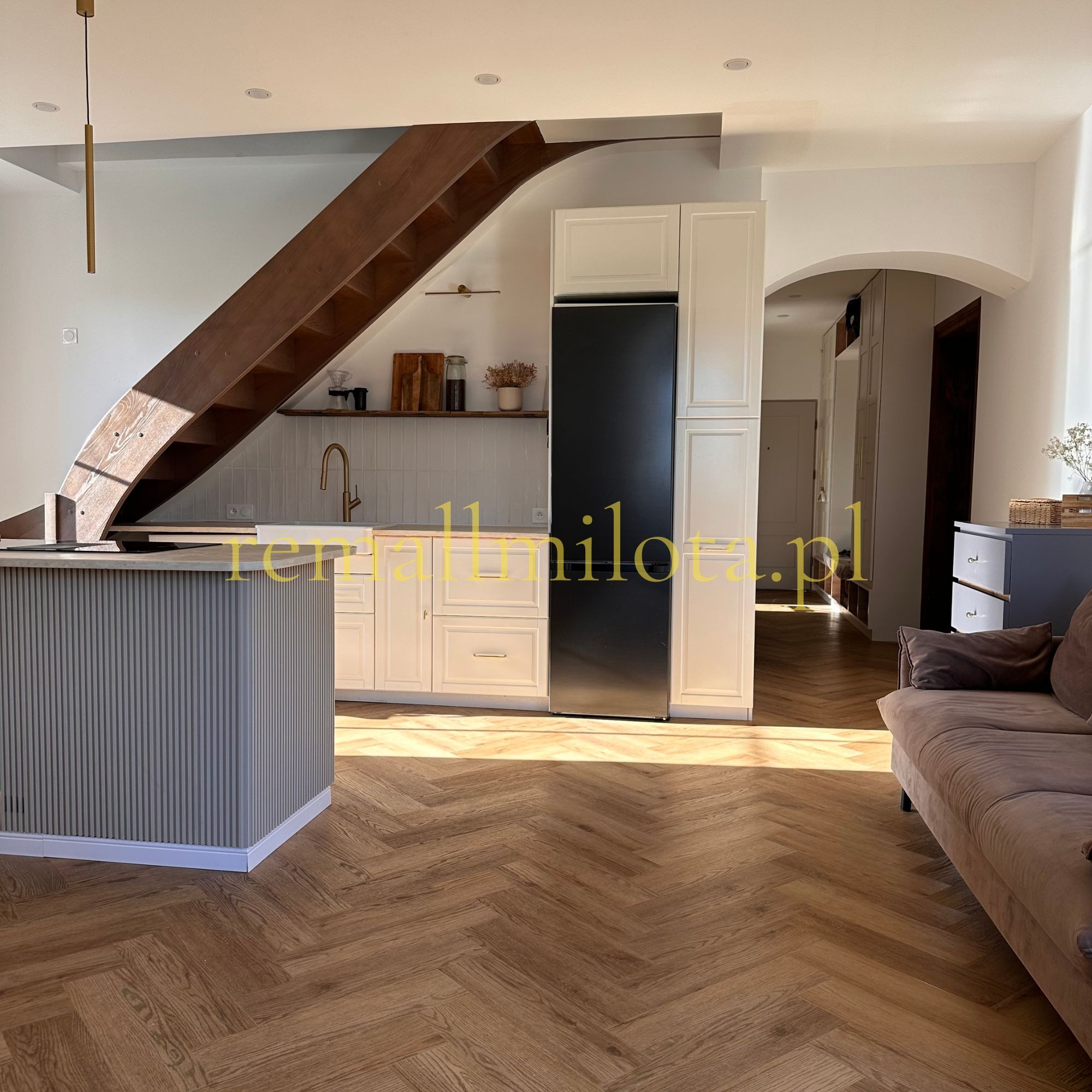 Jasne wnętrze po metamorfozie w Raciborzu: drewniana podłoga w jodełkę, schody z drewna, biała zabudowa kuchenna i wyspa. Nowoczesny design.