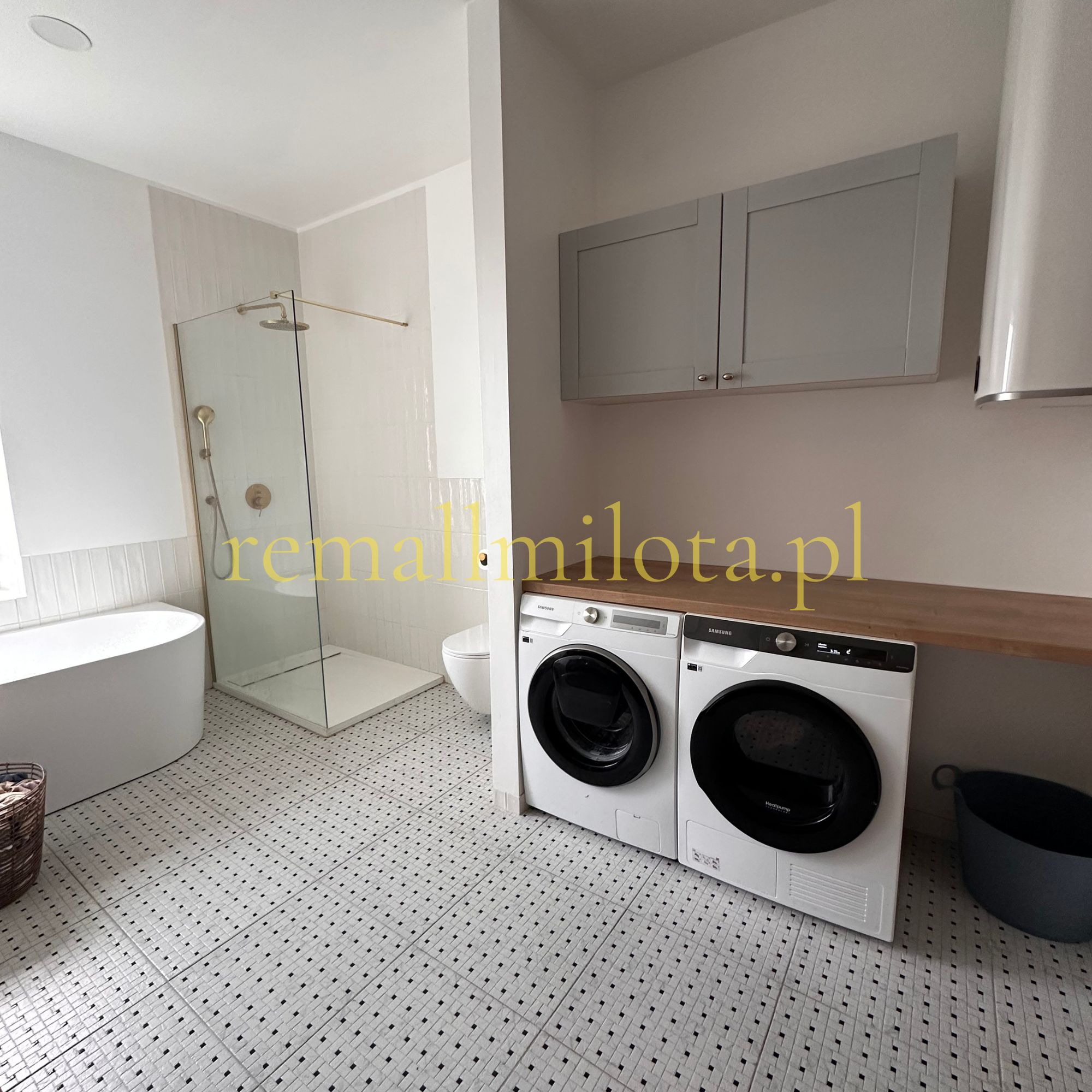 Jasna łazienka z kabiną prysznicową, wanną i pralko-suszarką Samsung. Biało-czarna podłoga w kratkę, szare szafki wiszące. Minimalistyczny design.
