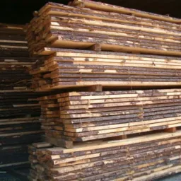 Stosy świeżo przetartego drewna z widoczną korą na krawędziach, ułożone na drewnianych paletach.