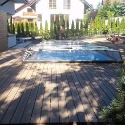 Firma Chrapla - Tarasy kompozytowe z zadaszeniem basenu, widok z poziomu gruntu, na pierwszym planie iglaki, w tle dom jednorodzinny i pracownik