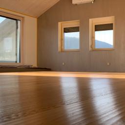 Firma Chrapla - Jasne, nowo wycyklinowane podłogi w pokoju z dwoma oknami z roletami i dużym oknem przesuwnym, widok na góry w tle.