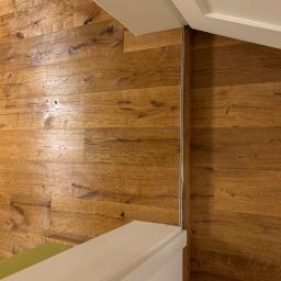 Firma Chrapla - Ułożona drewniana podłoga z wyraźnym usłojeniem, widoczne łączenie z białą listwą przypodłogową i fragmentem ściany.