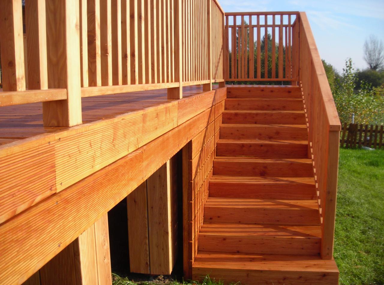 Nowy taras z drewna z balustradą i schodami, widok z boku, drewno w odcieniach pomarańczy, trawa w tle