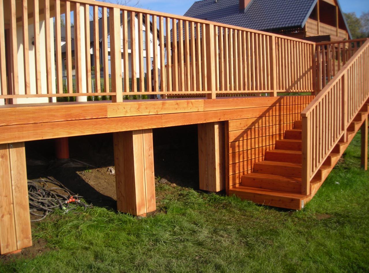 Nowy drewniany taras z balustradą i schodami, widok z boku, z przewodem ogrodowym leżącym pod spodem.