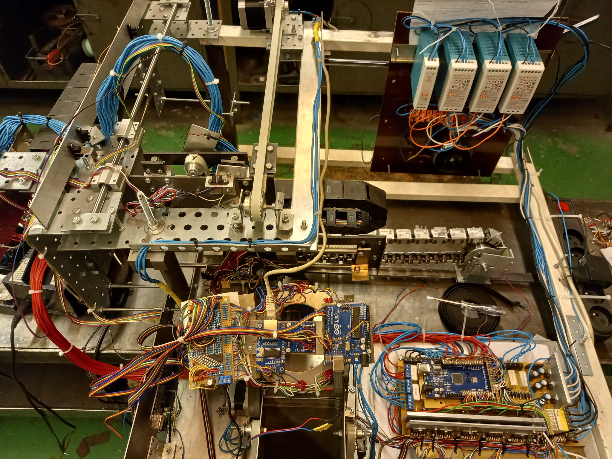 Skomplikowany układ elektroniczny z licznymi przewodami, płytkami Arduino, modułami zasilania i metalową konstrukcją, prawdopodobnie w trakcie budowy lub testowania.