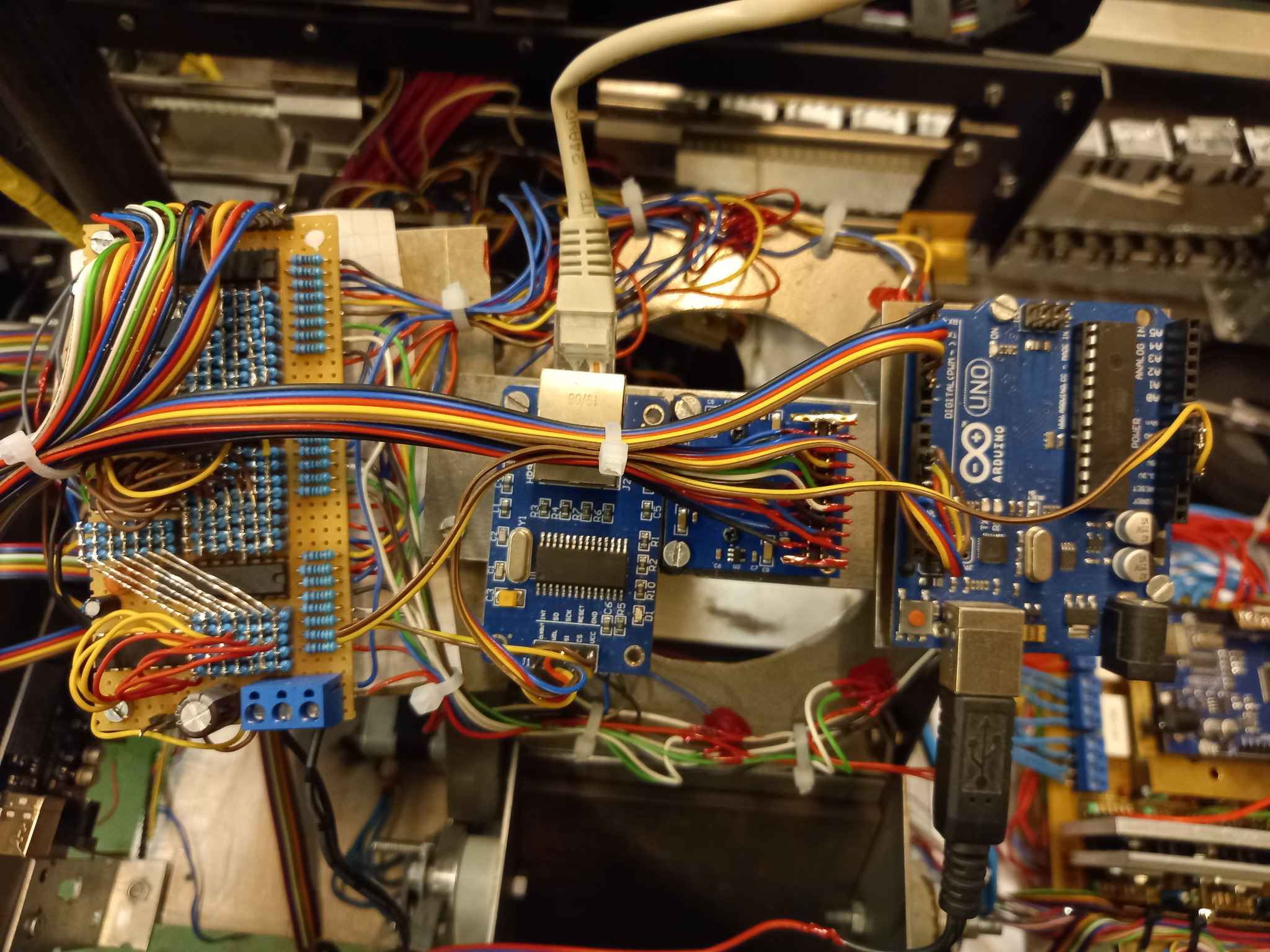 Widok z góry na skomplikowaną sieć połączeń elektrycznych na płytkach prototypowych, z widocznymi elementami Arduino Uno, rezystorami, kondensatorami i złączami, połączonych kolorowymi przewodami...
