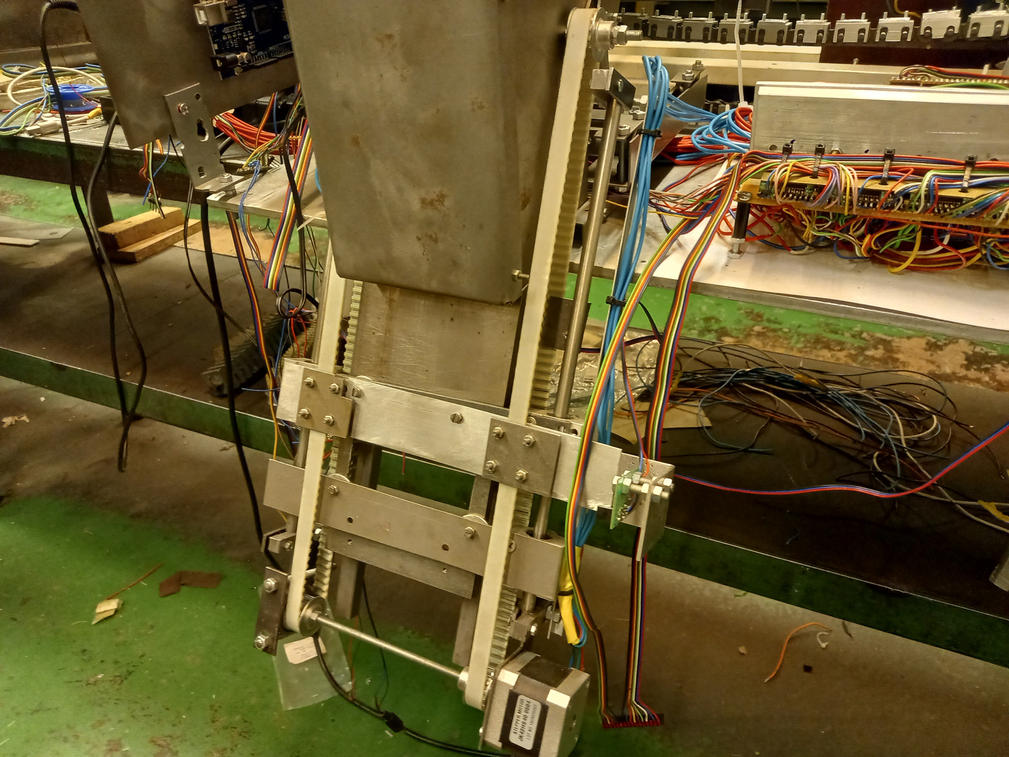 Detale konstrukcyjne urządzenia z widocznymi kablami i połączeniami elektrycznymi, silnik krokowy, metalowe elementy konstrukcyjne i przewody w różnych kolorach.