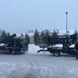 Eko Cleaning Serwis - Dwa podnośniki koszowe firmy Eko Cleaning Serwis na ośnieżonym placu podczas opadów śniegu. Widoczne numery kontaktowe i logo firmy na pojazdach.