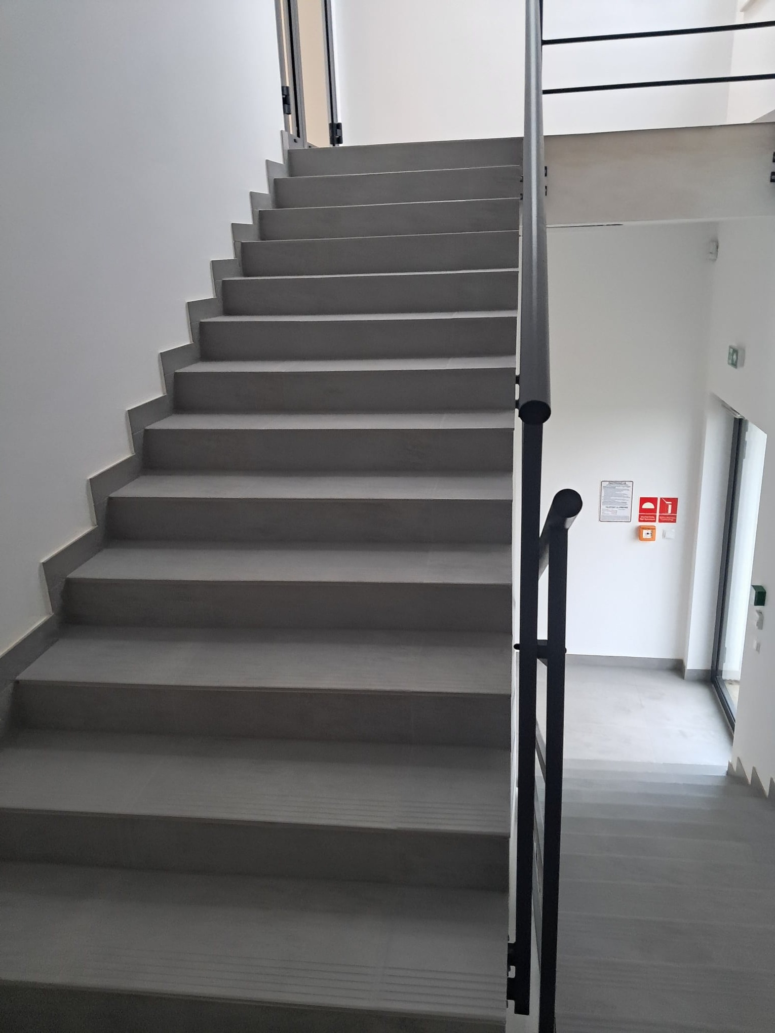 Nowoczesne, szare schody z metalową balustradą w jasnym wnętrzu budynku, widok z dołu na górę.