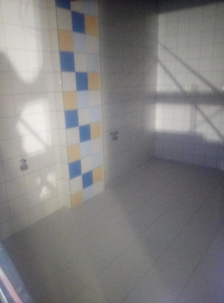 Wnętrze łazienki w trakcie remontu z fragmentem ściany wyłożonej biało-niebiesko-żółtą mozaiką z płytek ceramicznych i widocznymi przyłączami hydraulicznymi.