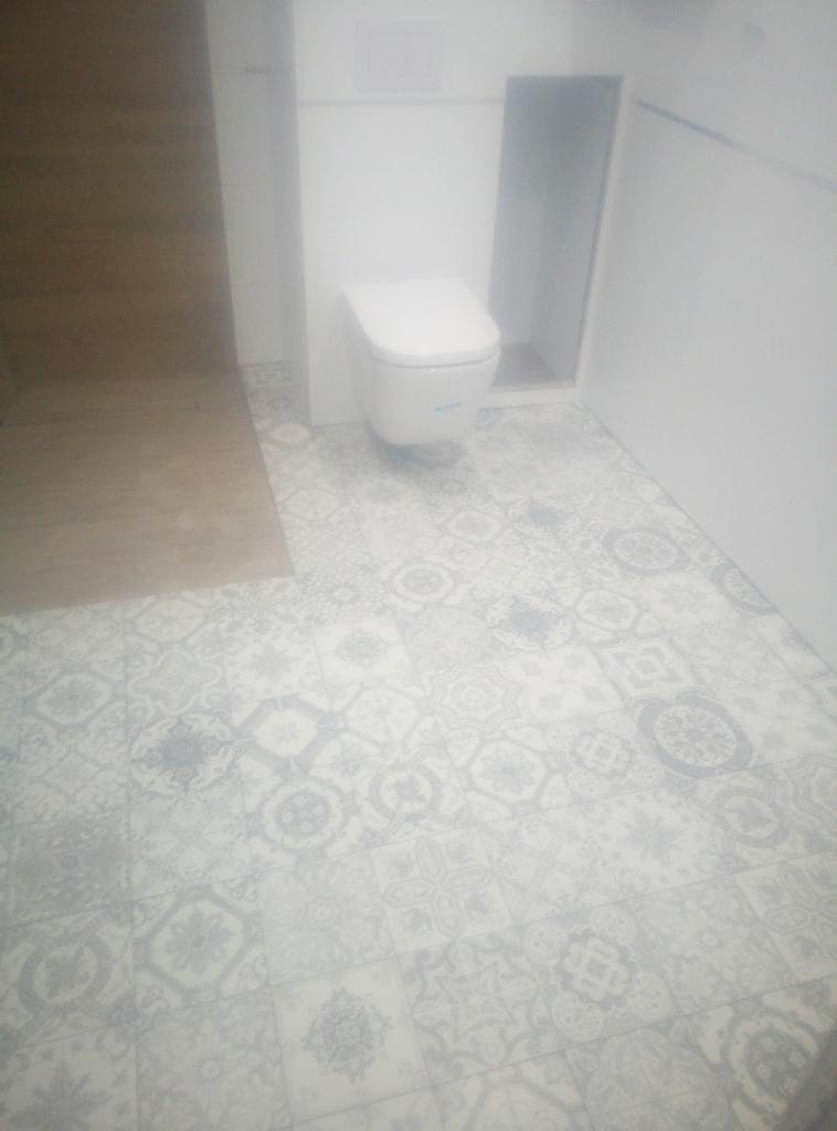 Wnętrze łazienki z toaletą podwieszaną i wzorzystą, szaro-białą podłogą z płytek ceramicznych.