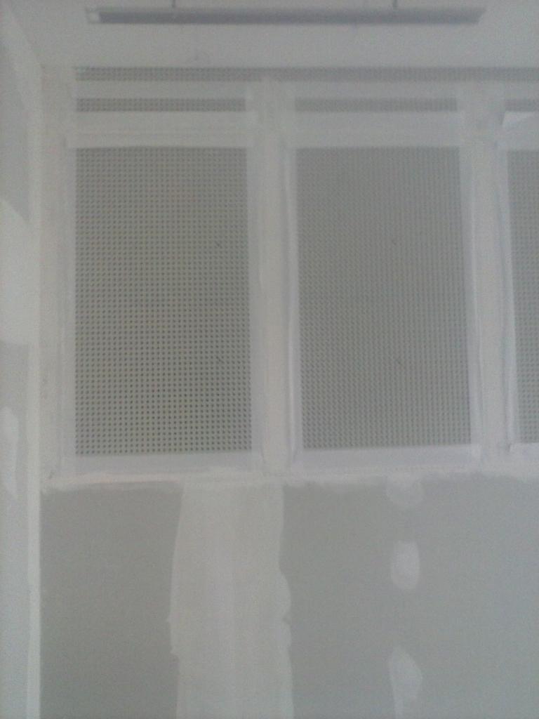 Fragment ściany z zamontowaną perforowaną płytą, widoczne niedoskonałości w szpachlowaniu łączeń, przygotowanie do dalszych prac wykończeniowych.