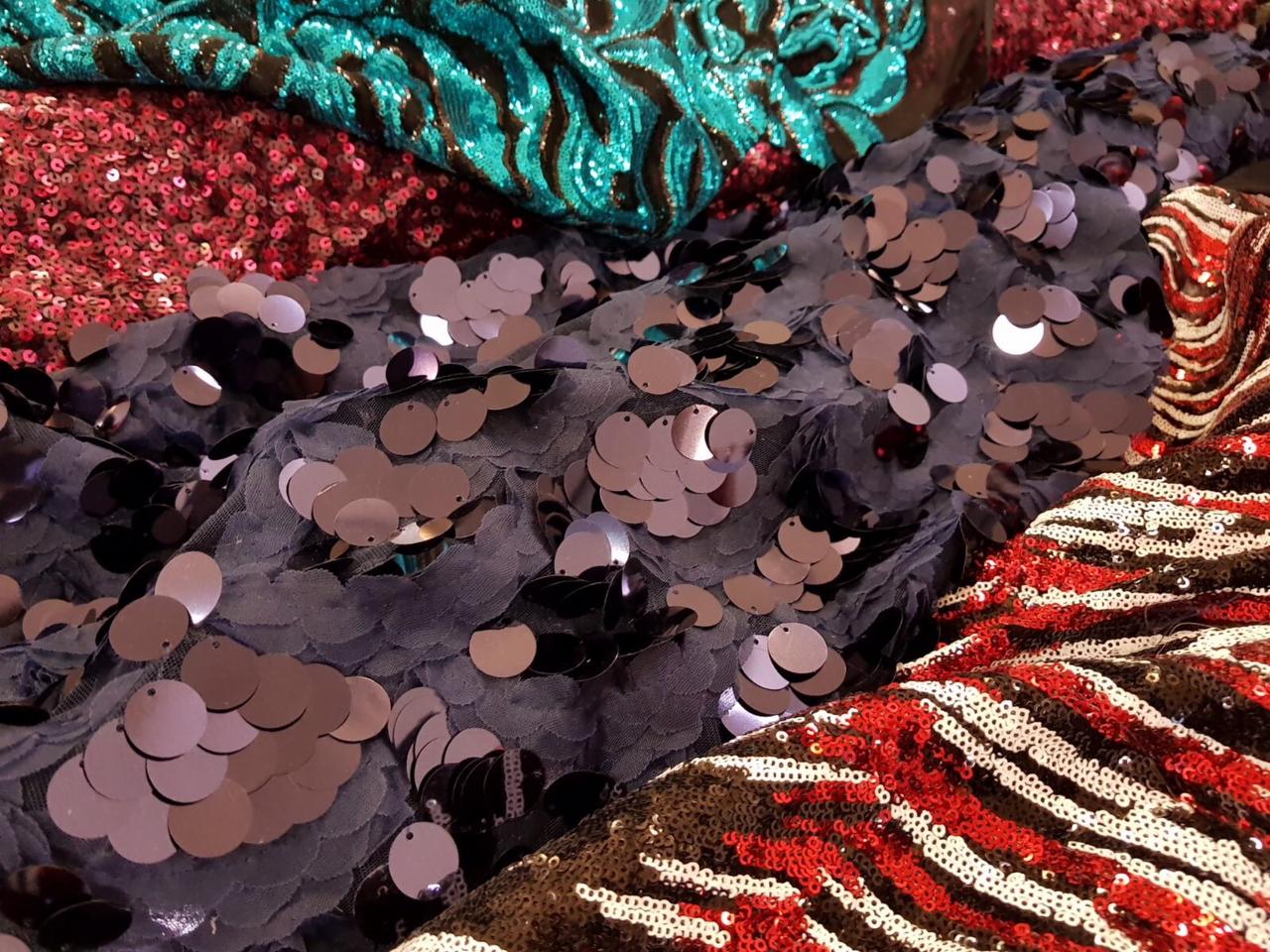 Różnorodność tkanin z cekinami w odcieniach turkusu, różu, granatu i czerwieni w zwierzęce wzory, ułożone warstwowo.