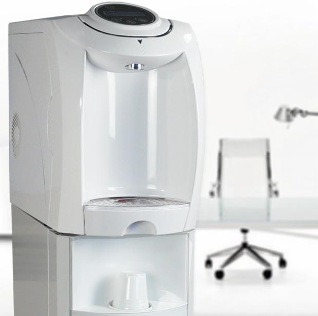Biały dystrybutor wody w biurze, z plastikowym kubkiem w dolnej części i krzesłem biurowym w tle.