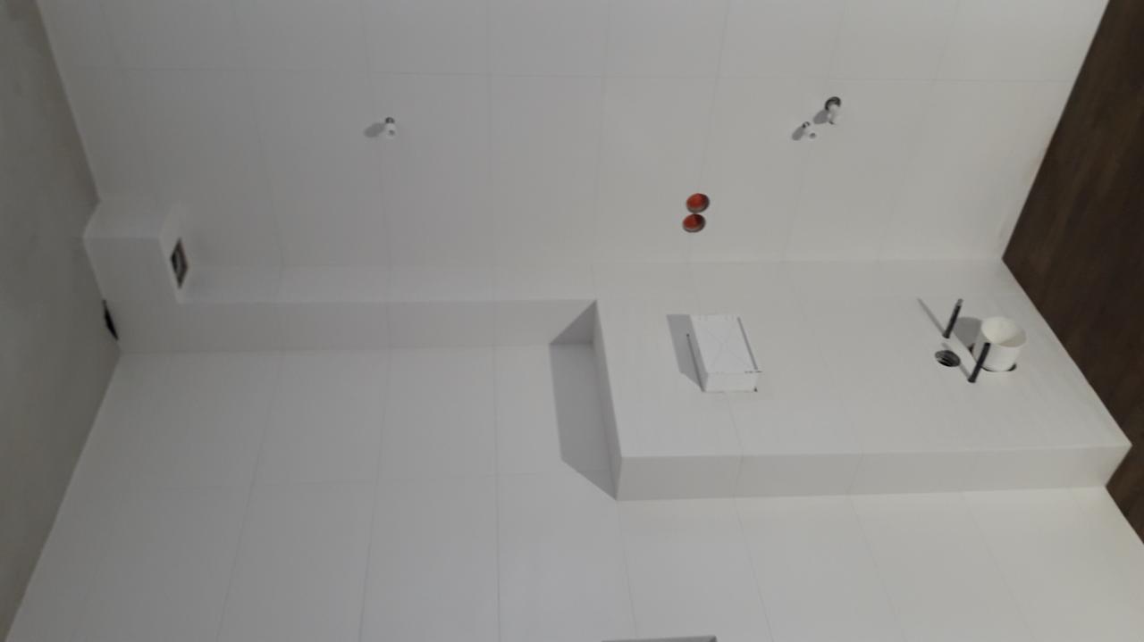 Wykończona, biała łazienka w Mielcu z równo ułożonymi, błyszczącymi płytkami, widoczne otwory na oświetlenie i elementy instalacji hydraulicznej oraz narożne półki.