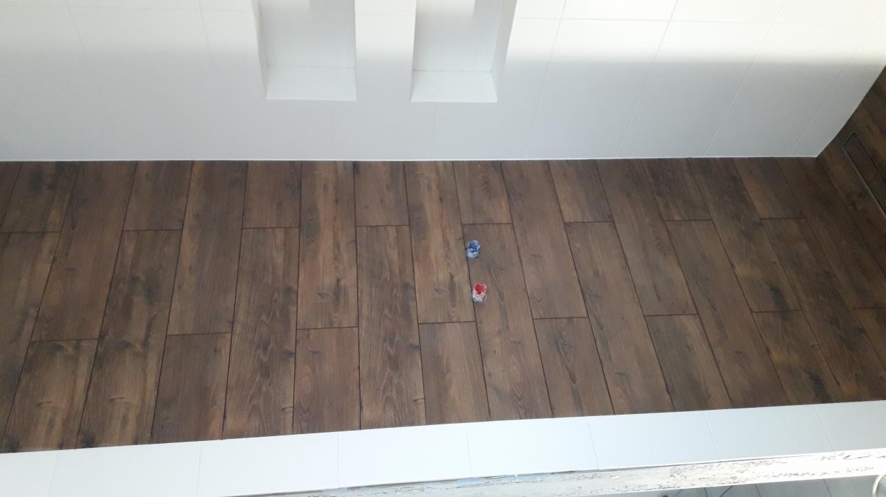 Ułożony parkiet w łazience z widocznymi dwoma puszkami po farbie na podłodze, białe płytki na suficie i ścianach.