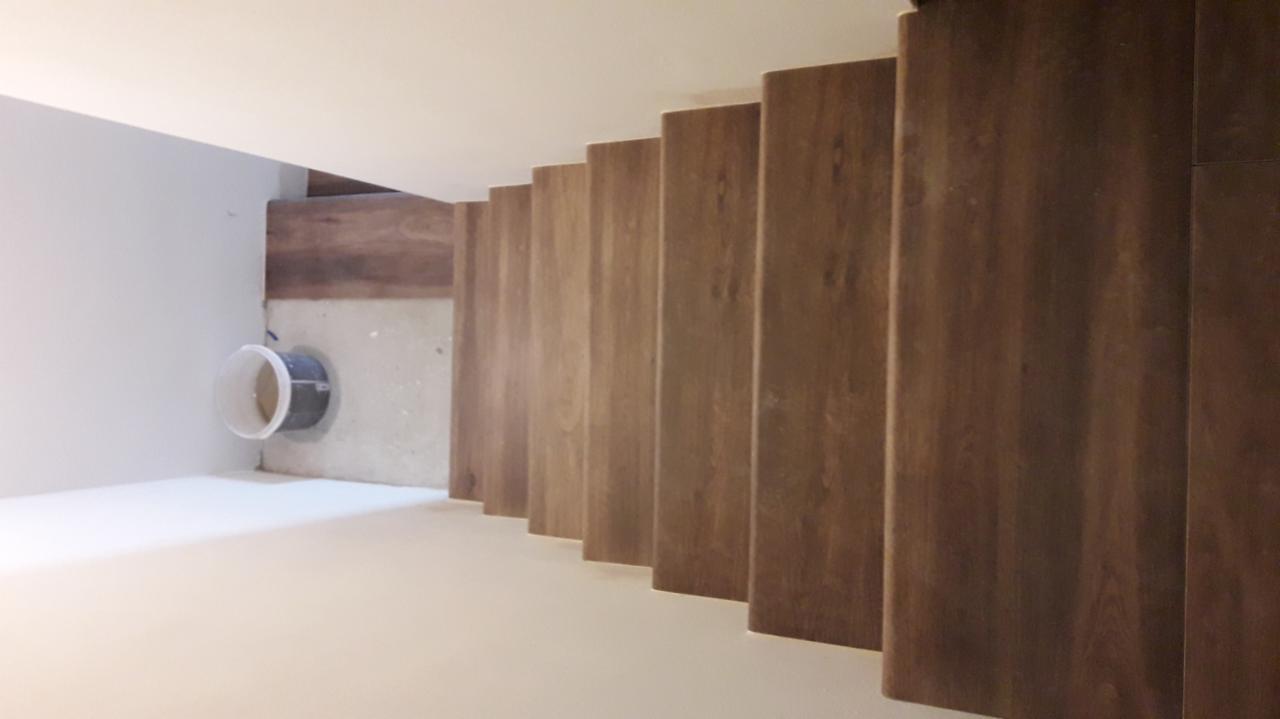 Montaż drewnianych paneli na schodach, widok z góry, widoczna instalacja w ścianie zabezpieczona plastikowym wiaderkiem.