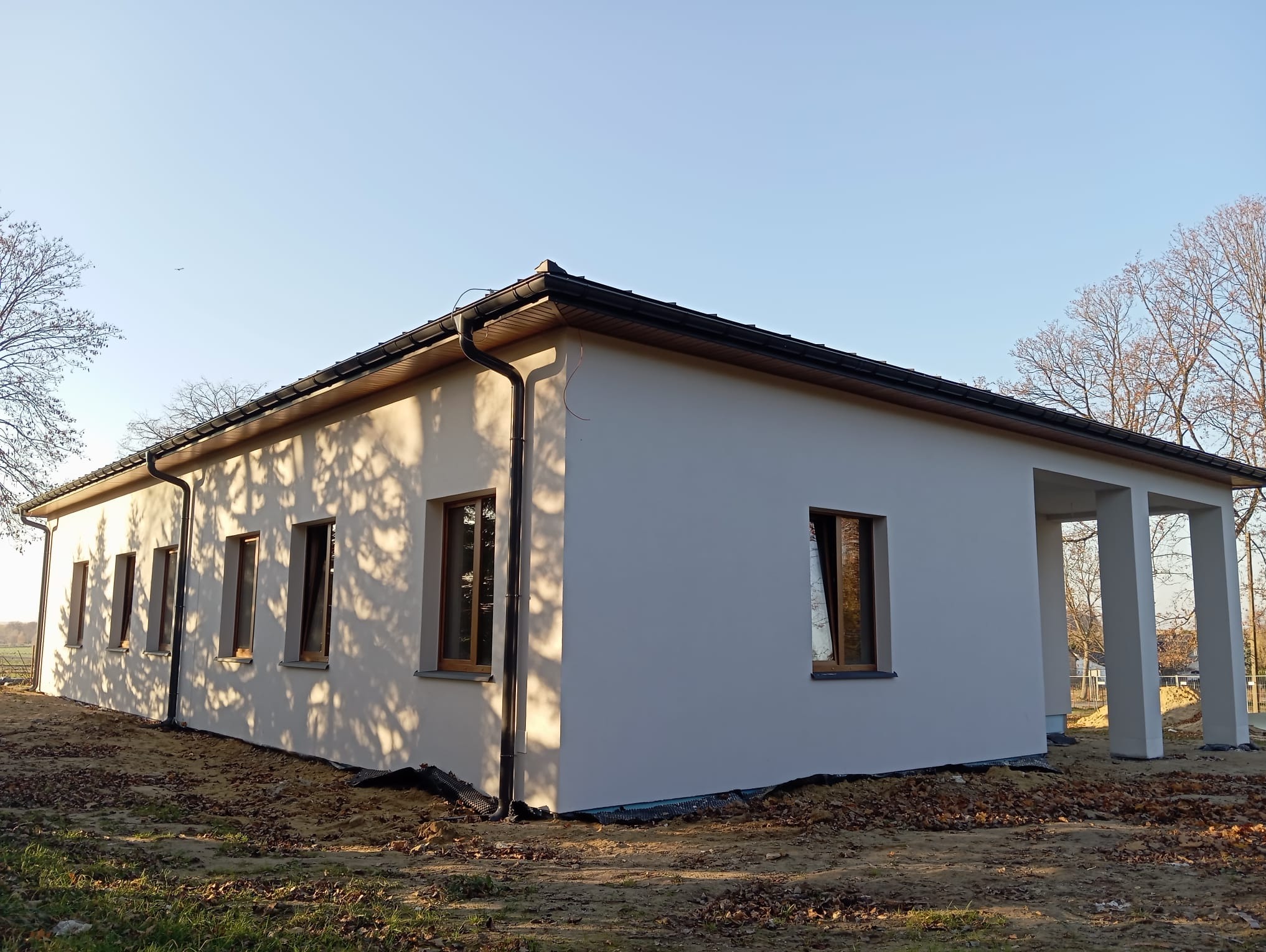 Nowoczesny, parterowy dom w Lublinie z jasną elewacją, ciemnym dachem i drewnianymi oknami, widziany z zewnątrz w słoneczny dzień.