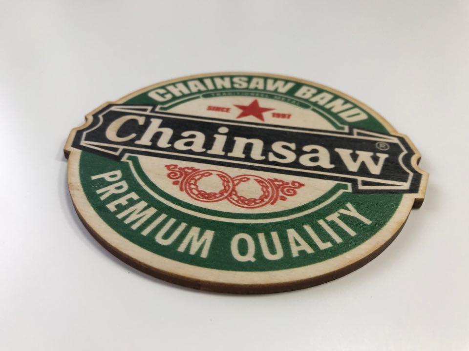 Okrągła drewniana naklejka z nadrukiem w stylu logo piwa, z napisem Chainsaw Band i Premium Quality, leżąca na białym tle.
